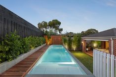 an empty swimming pool surrounded by greenery next to a wooden fence and brick building