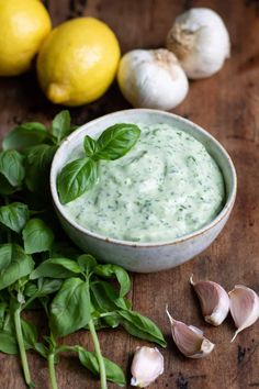 a bowl filled with green sauce next to garlic and lemons on a wooden table