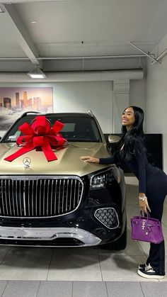 a woman standing next to a car with a large red bow on it's hood