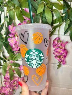 a starbucks cup with hearts and basketballs on it is being held up by a woman's hand