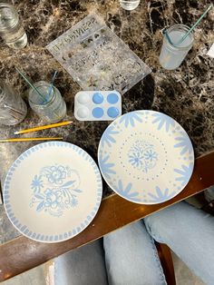 two plates with blue and white designs sit on a table next to paintbrushes