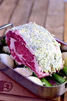 a piece of meat and vegetables in a metal container on a wooden table with utensils