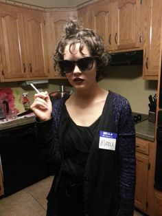 a woman wearing sunglasses and holding a toothbrush in her hand while standing in a kitchen