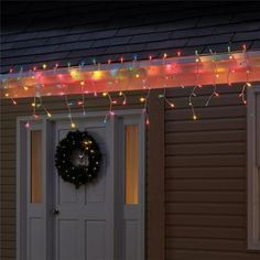 a christmas wreath on the front door of a house with lights hanging from it's side