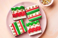 four decorated cookies on a pink plate next to some gold and green beads, with a bowl of candy in the background