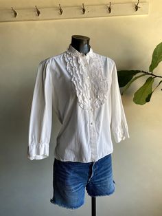 "Vintage 1970s Unbranded White Cotton Ruffle Blouse. White in color made from cotton fibers. Brand is unknown (tag has been cut). Long sleeve blouse with ruffled accents along front. Button down closure along front and cuffs. Overall condition of garment is good with only minor flaws that include; blouse is missing one of the buttons on the right cuff as shown in photos. No rips, tears, or staining. Please see all photos for details. Refer to measurements below to ensure a proper fit (modeled on Classic Cotton Top With Ruffled Collar, Classic Cotton Tops With Ruffles, Fitted Shirt With Ruffled Collar For Daywear, Ruffled Collar Button Top For Daywear, Vintage Lace Collar Button-up Top, Victorian Cotton Blouse With Lace Collar, Fitted Cotton Shirt With Ruffled Collar, Victorian Cotton Tops For Spring, Victorian Cotton Tops For Summer