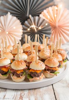 mini burgers with toothpicks are arranged on a platter for an appetizer