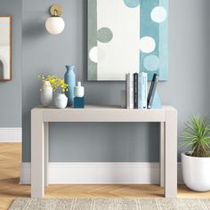 a table with books and vases on it in front of a wall mounted painting