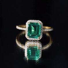 an emerald and diamond ring sitting on top of a black surface with diamonds around it