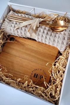 a wooden cutting board in a box with utensils and napkins on it