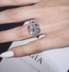 a woman's hand with a diamond ring on her finger and white nail polish