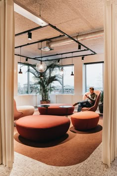 a man sitting on a couch in a room with large windows and round seating area