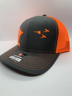 Richardson 112 dark gray/neon orange snap back hat with orange vinyl decal of Minnesota and hunter with dog on left and pheasants flying on rightMade to order Orange Trucker Snapback Hat, Orange Snapback Trucker Hat For Outdoor, Orange Trucker Hat For Sports, Adjustable Orange Trucker Hat, Orange Curved Brim Trucker Hat For Outdoor, Orange Adjustable Trucker Hat With Curved Bill, Orange Snapback Trucker Hat For Sports, Outdoor Orange Snapback Hat, Orange Snapback Hat For Outdoor