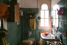 a green tiled bathroom with a sink, toilet and window in the corner on the wall