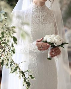 a woman in a white wedding dress holding a bouquet of flowers and wearing a veil