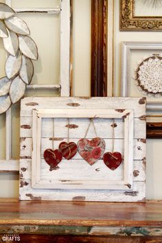 an old frame with hearts hanging from it on a table next to other framed pictures