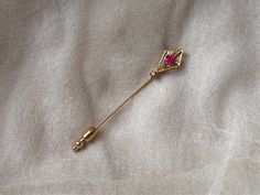 "This enchanting stick pin features a glittering, faceted lab-made ruby stone set in a delicately etched 10k gold arts-and-crafts style setting with a seed pearl at the bottom. It is marked on the pin portion as being 10k gold along with a partial  maker's mark that is hard to read.  It weighs 1.05 g (without fob), measures 2.5\" x 3/8\" and is in great antique condition." Art Deco Ruby Jewelry Gift, Art Deco Ruby Jewelry As A Gift, Elegant Brooch For Valentine's Day, Elegant Valentine's Day Brooch Jewelry, Elegant Valentine's Day Brooch, Elegant Wedding Pins For Valentine's Day, Art Deco Gold Brooches As Gift, Gold Art Deco Brooches As A Gift, Elegant Gold Brooch For Valentine's Day