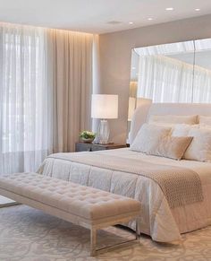 a large white bed sitting in a bedroom next to a window with curtains on it