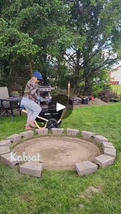 a man sitting in the middle of a yard using a wheelbarrow to build a fire pit