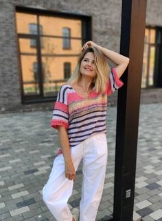 a woman standing next to a pole with her hands on her head and wearing white pants