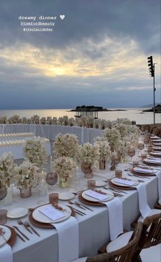 a long table set up with white flowers and place settings for dinner at the beach