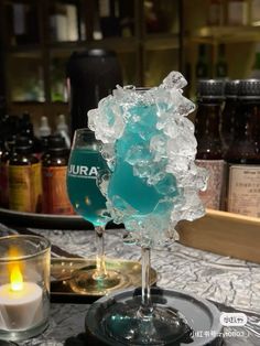 a glass filled with ice sitting on top of a table next to candles and bottles