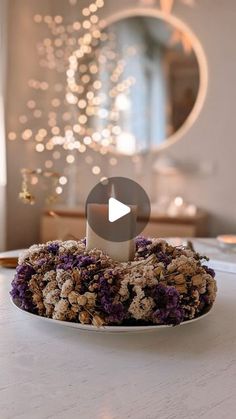 a white plate topped with purple flowers on top of a table next to a mirror