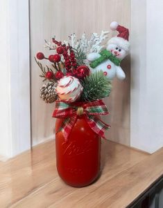 a red mason jar filled with christmas decorations on top of a wooden shelf next to a wall