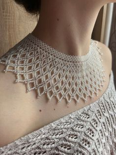 a woman wearing a white crochet necklace on her neck and shoulder, looking out the window