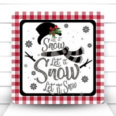 a snow let it snow sign hanging on the side of a white brick wall with red and black checkered tablecloth