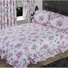 a white bed with pink and purple flowers on the comforter is in front of a window