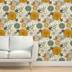 a white couch sitting in front of a wall with yellow and green flowers on it