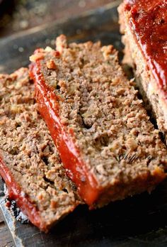 two slices of meatloaf with ketchup are on a wooden cutting board