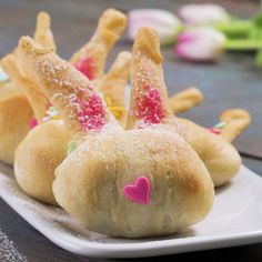 small pastries with pink and green decorations on a white plate sitting on a wooden table