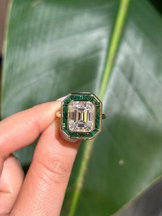 a woman's hand holding a ring with an emerald center surrounded by white diamonds