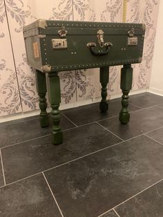 a green trunk sitting on top of a wooden table in front of a wallpapered wall