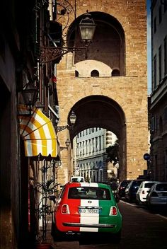 a red, white and green car parked in front of an arch