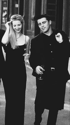 black and white photograph of two people walking down the street with drinks in their hands