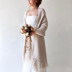 a woman in a white dress holding a bouquet of flowers and wearing a cardigan