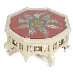 a red and white table with ornate designs on the top, sitting in front of a gray background