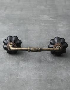 an antique brass handle with black flowers on the top and bottom, sitting on a concrete surface