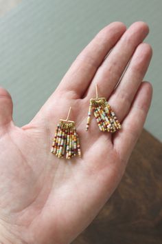 a person's hand holding two small beaded earrings