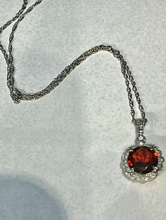 14K White Gold Diamond & Garnet scalloped Halo fancy pendant. This Halo pendant features a beautiful faceted 2.18ct round 8mm red Garnet stone, surrounded by diamonds, 0.05ctw. the chain is a 14K white gold rope chain, 1mm, 18" longThe arrangement of its facets is similar to that of a round brilliant, designed to maximize light and color. The sides are fancy scroll work with an open back. The stone is set in a 14K white gold prong setting which has an attractive halo design and holds the garnet Fine Jewelry: Brilliant Cut Garnet, Red Diamond Necklace With Halo Setting, Fine Jewelry With Brilliant Cut Garnet, Fine Jewelry Garnet With Brilliant Cut, Elegant Garnet Jewelry With Brilliant Cut, Red Round Necklace With Brilliant Cut, Red Round Necklaces With Brilliant Cut, Round Garnet Jewelry With Halo Setting, Red Round Cut Elegant Necklace