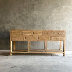 an old wooden dresser with drawers in front of a gray wall and concrete flooring