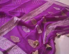 A Handwoven Purple Banarasi Georgette Kadhuwa Saree to make you stand out in a crowd. Furthermore, the saree is weaved all over with golden & silver zari in a beautiful kadhuwa weave pattern. Thus, this saree is for those who love handloom and have a taste for traditional attire. Also, it comes with blouse piece. Note: Banarasi Khaddi Georgete is a very soft and drapy fabric. Additional Information Color : Purple Zari Color: Golden and Silver Technique: Banarasi Kadhuwa Weaving Fabric: Pure Khad Elegant Katan Silk Saree With Gota Work, Traditional Silver Dupatta With Gota Work, Silver Silk Dupatta For Festivals, Tussar Silk Saree With Gota Work For Celebrations, Celebration Tussar Silk Saree With Gota Work, Banarasi Silk Dupatta With Gota Work For Celebration, Silver Handloom Dupatta For Festivals, Celebration Tussar Silk Dupatta With Gota Work, Silver Handloom Dupatta For Festive Occasions