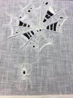 an embroidered spider web with holes in the center on a piece of fabric, and black dots at the bottom