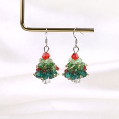 a pair of green and red beaded christmas tree earrings hanging from a metal hook