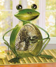 a green frog sitting on top of a table next to a fan with eyes closed