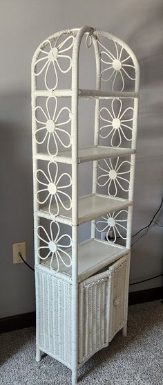 a white wicker shelf with drawers and shelves on the bottom, in front of a gray wall