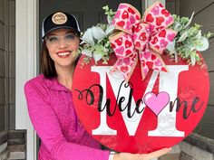 a woman holding up a welcome sign with flowers in the center and a bow on it